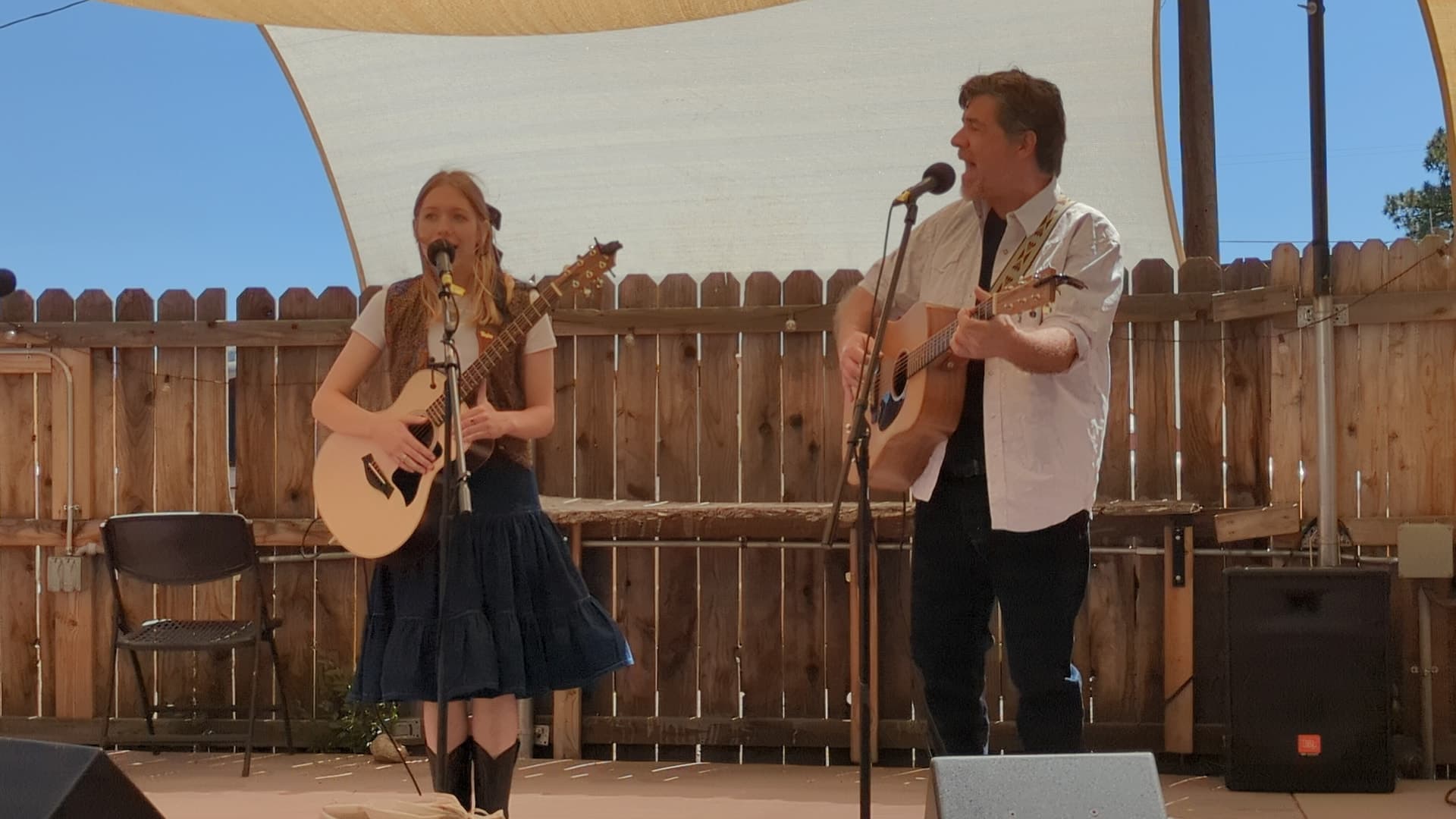 Tatum and Chad singing and playing acoustic guitars together on an outdoor stage.
